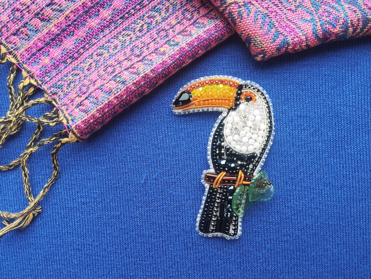 a close-up of a colorful bird brooch, specifically a toucan, set against a blue background.