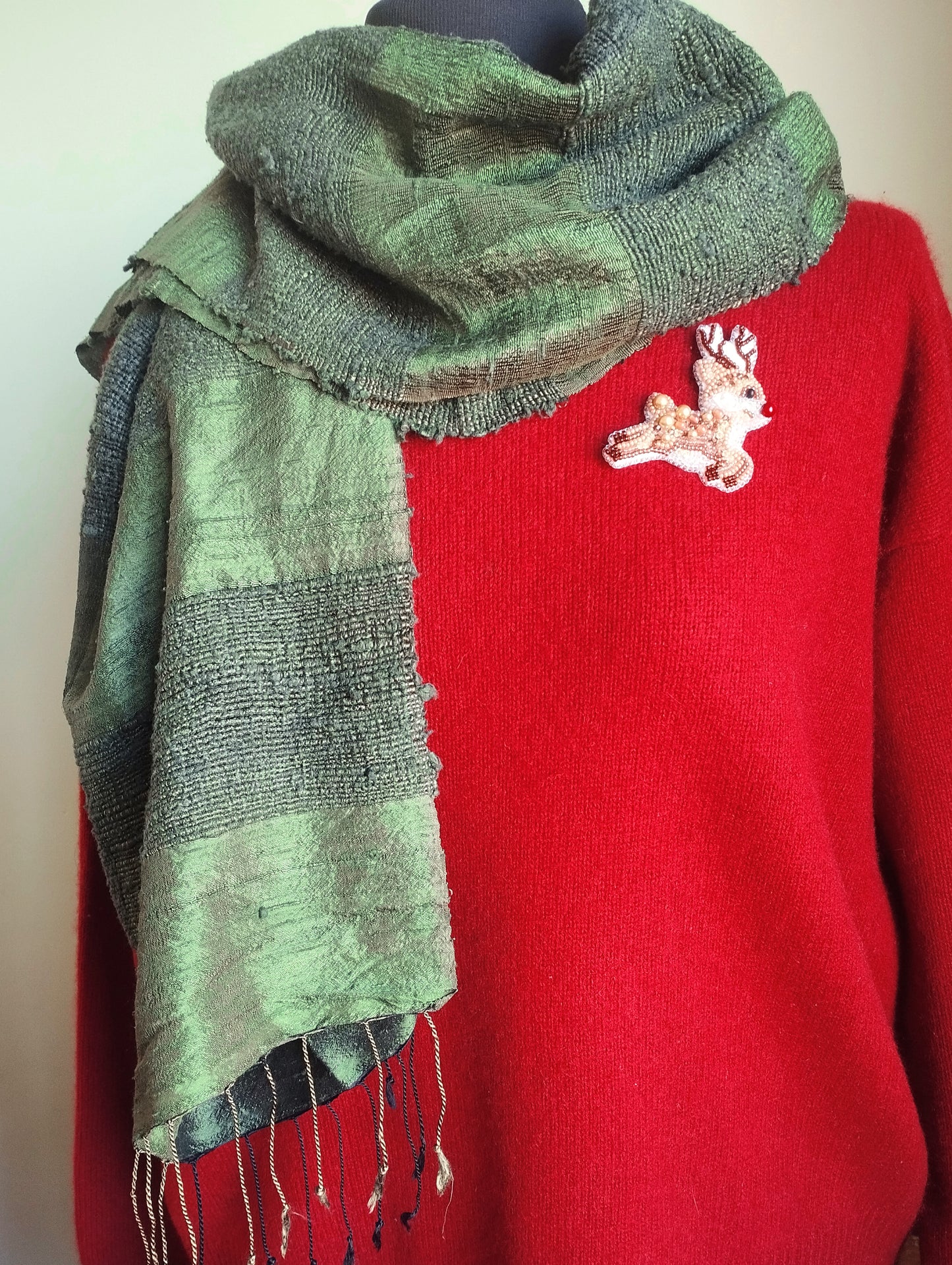 A red sweater with a green and black scarf draped over it, and a small embroidered patch on the sweater.