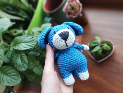 a hand holding a small blue crocheted teddy bear