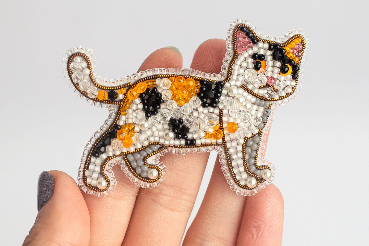 A hand holding a decorative beaded cat pin.