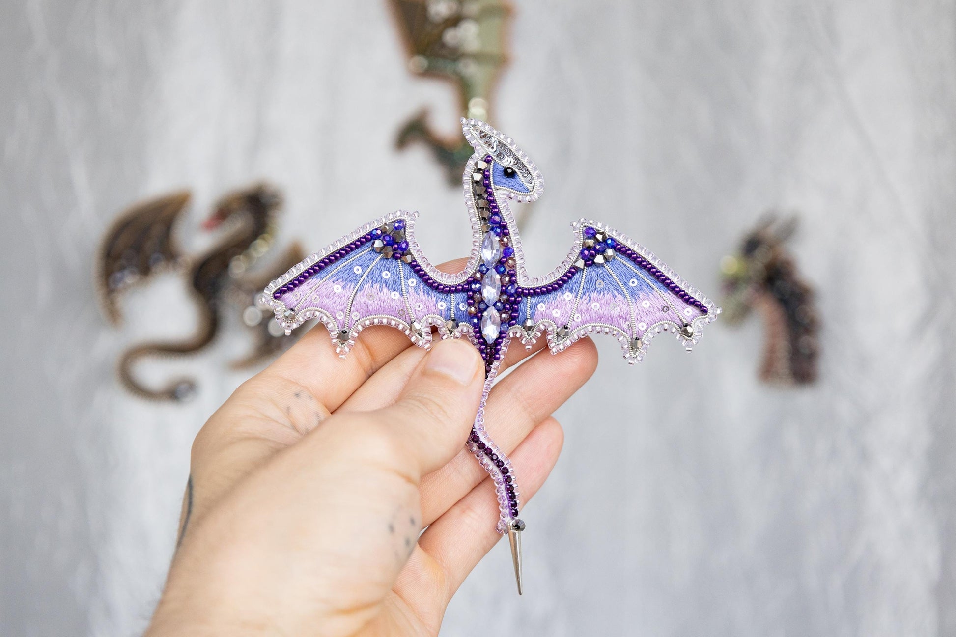 a hand holding a purple and blue dragon brooch