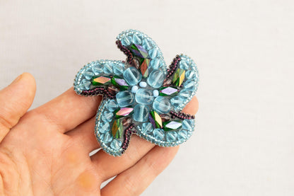 a hand holding a small blue flower brooch