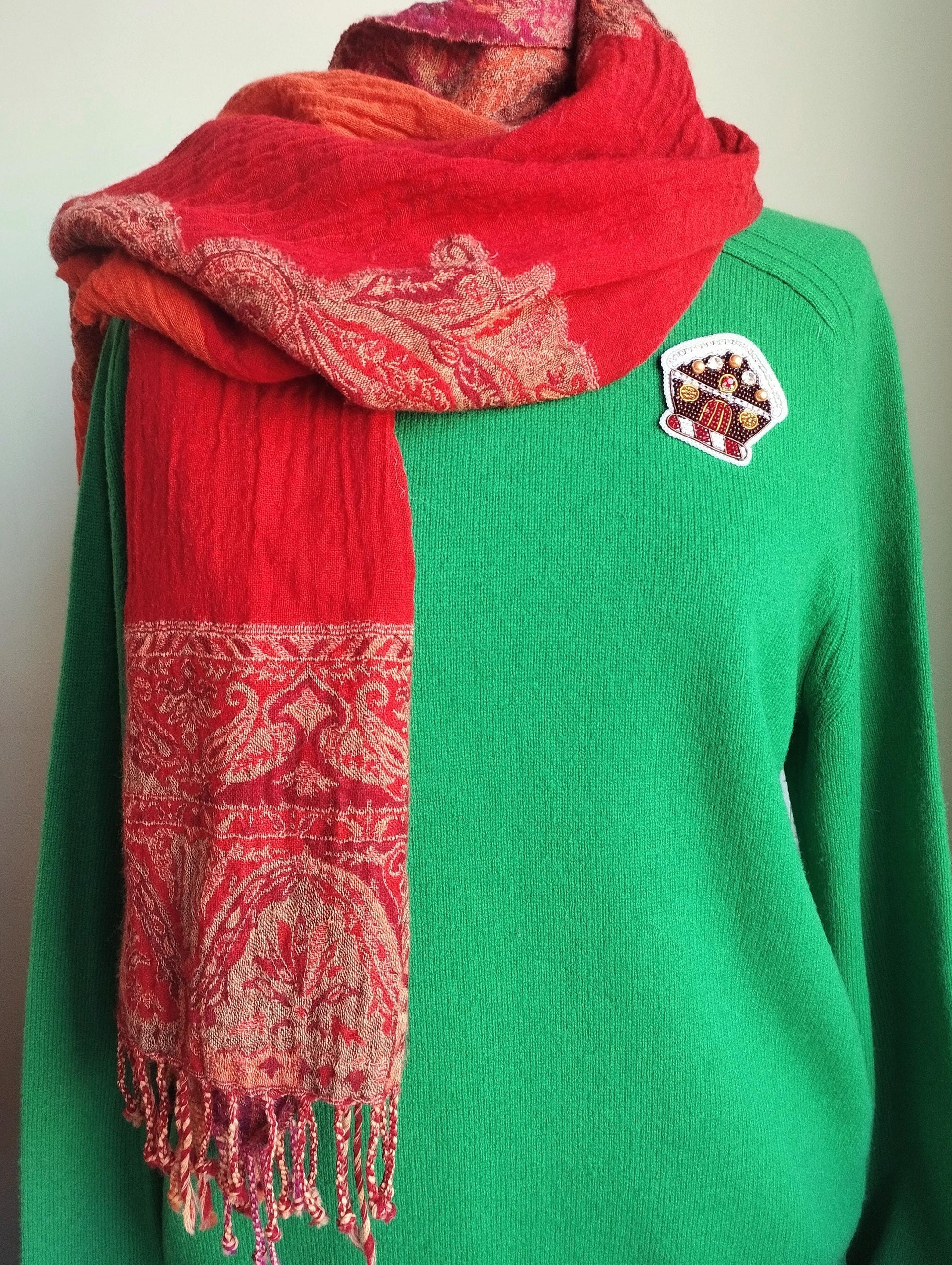 A person wearing a green sweater and a red and orange patterned scarf.