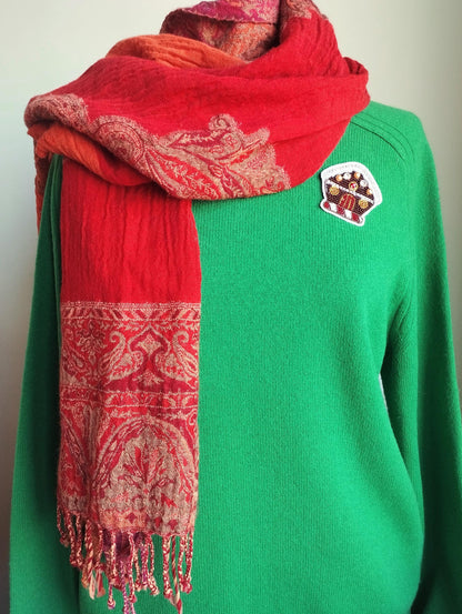A person wearing a green sweater and a red and orange patterned scarf.