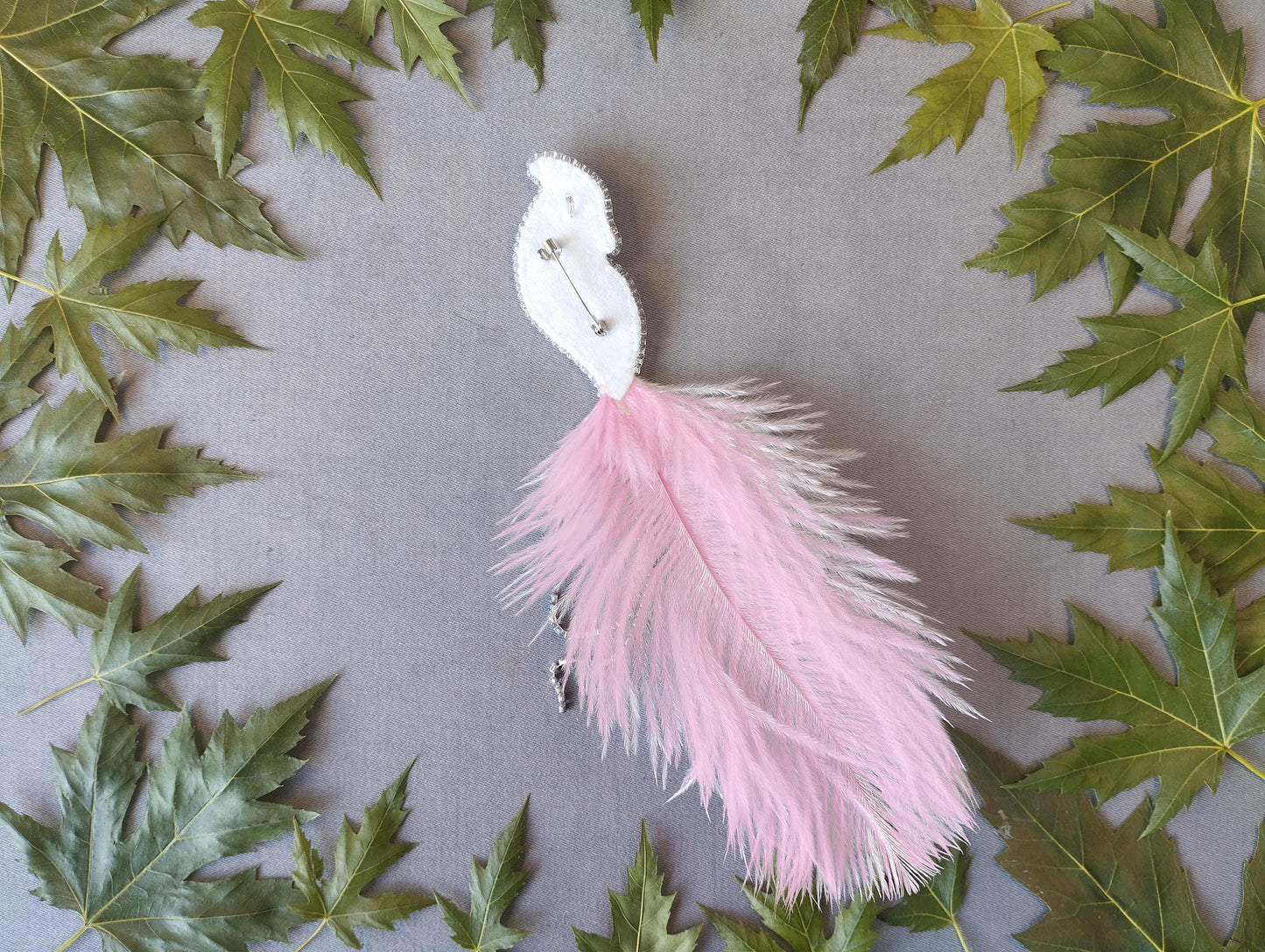 a white feather pin surrounded by green leaves on a gray background.