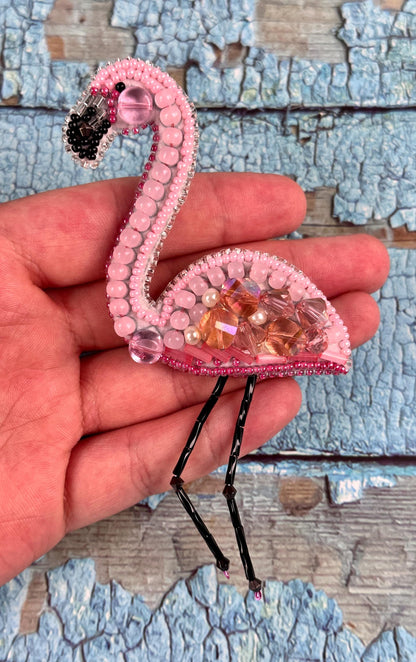 a pink flamingo brooch sitting on top of a persons hand