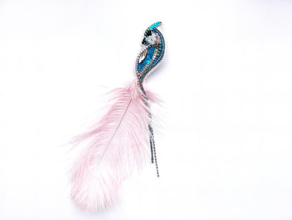 A decorative feather with a blue and green design, possibly made of beads or sequins, is shown against a white background.