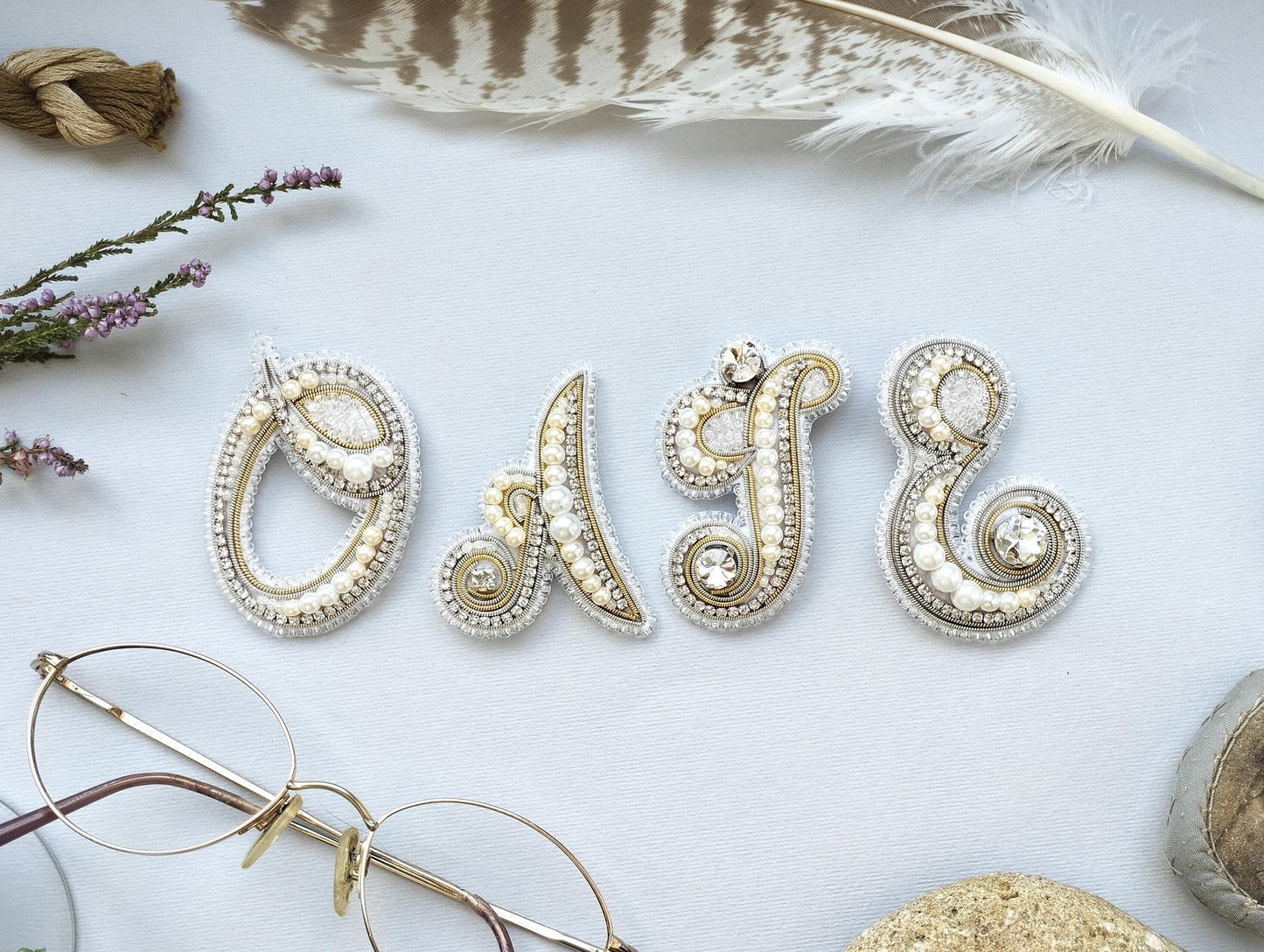 a close-up of a white background with various decorative elements, including a feather, a pair of glasses, and a name spelled out using beads and pearls.