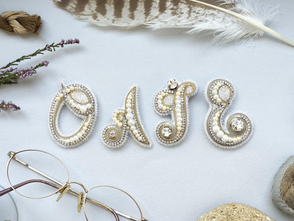 a close-up of a white background with various decorative elements, including a feather, a pair of glasses, and a name spelled out using beads and pearls.