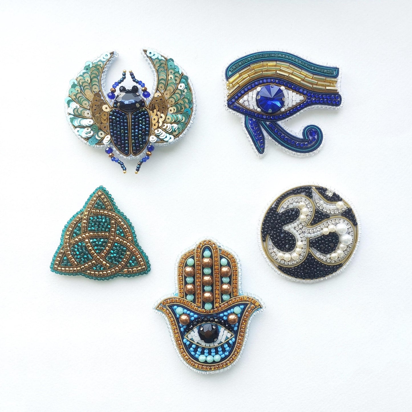 five ornate brooches or pins, each featuring intricate designs and embellishments. The brooches are arranged in a row against a white background, showcasing their detailed craftsmanship and artistic appeal.