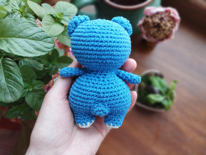 a hand holding a small crocheted blue teddy bear