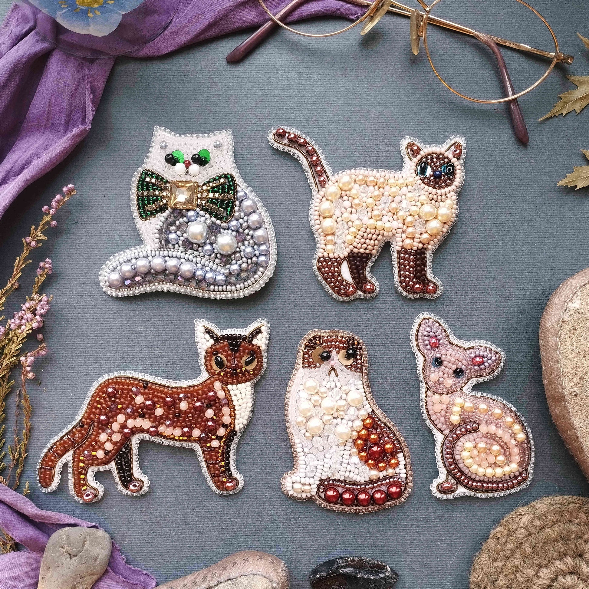six decorative cat brooches made of beads, arranged on a gray background.