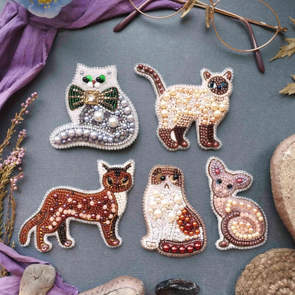 six decorative cat brooches made of beads, arranged on a gray background.