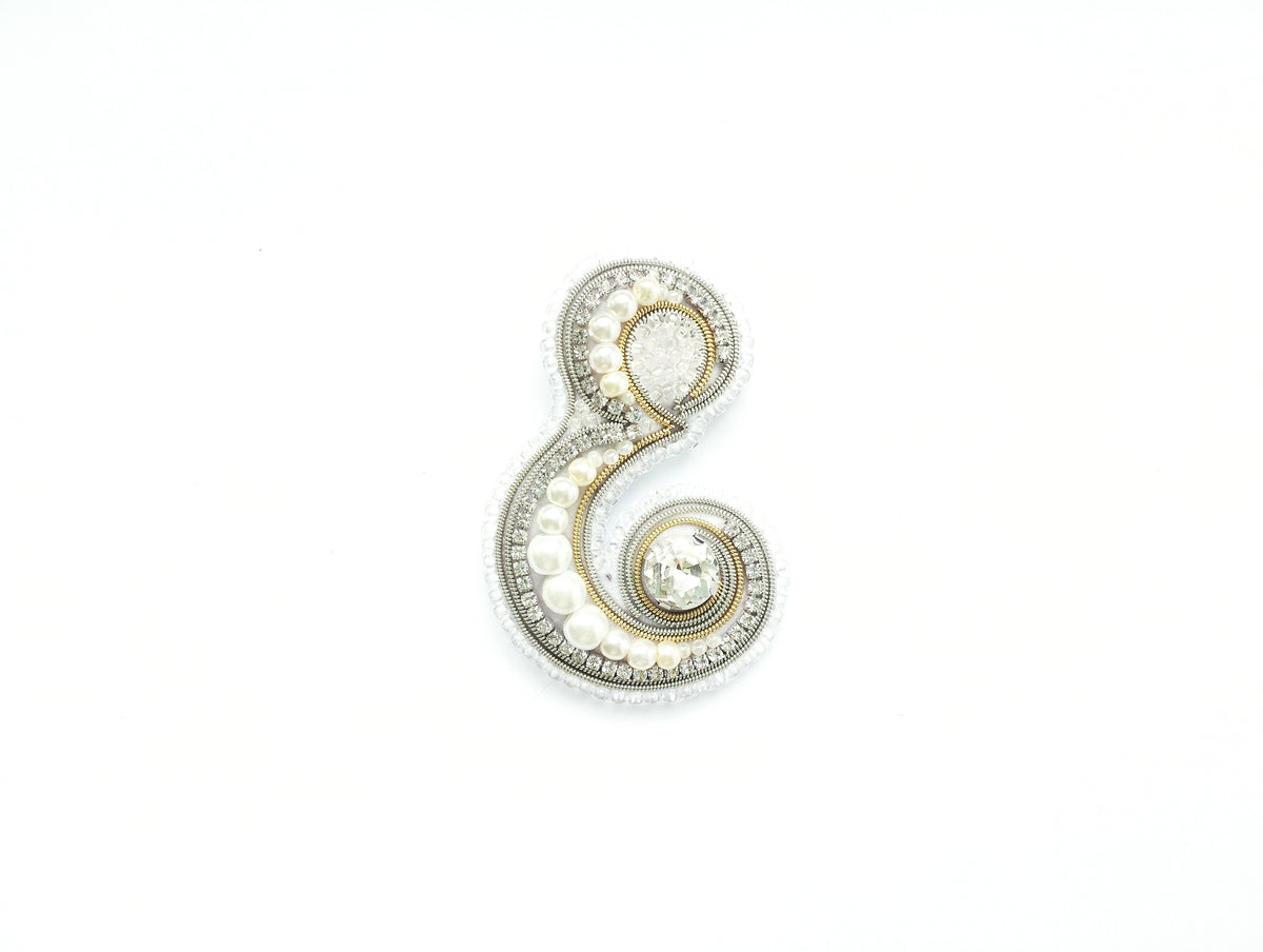 A decorative piece made of various materials, including pearls, diamonds, and other embellishments, forming the letter 'E' on a white background.
