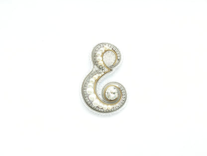 A decorative piece made of various materials, including pearls, diamonds, and other embellishments, forming the letter 'E' on a white background.