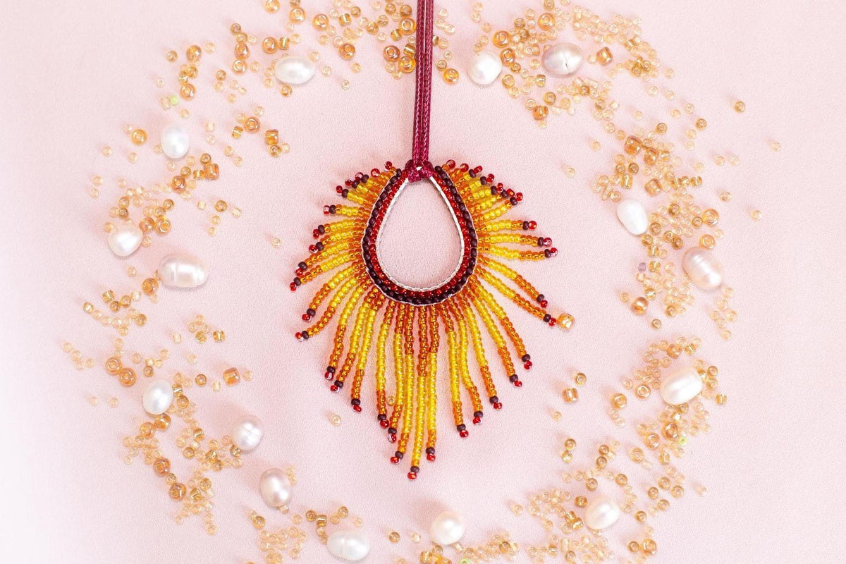 a vibrant, beaded necklace with a large, sun-like pendant surrounded by an array of small, round, and round beads in various colors, including gold, white, and red.