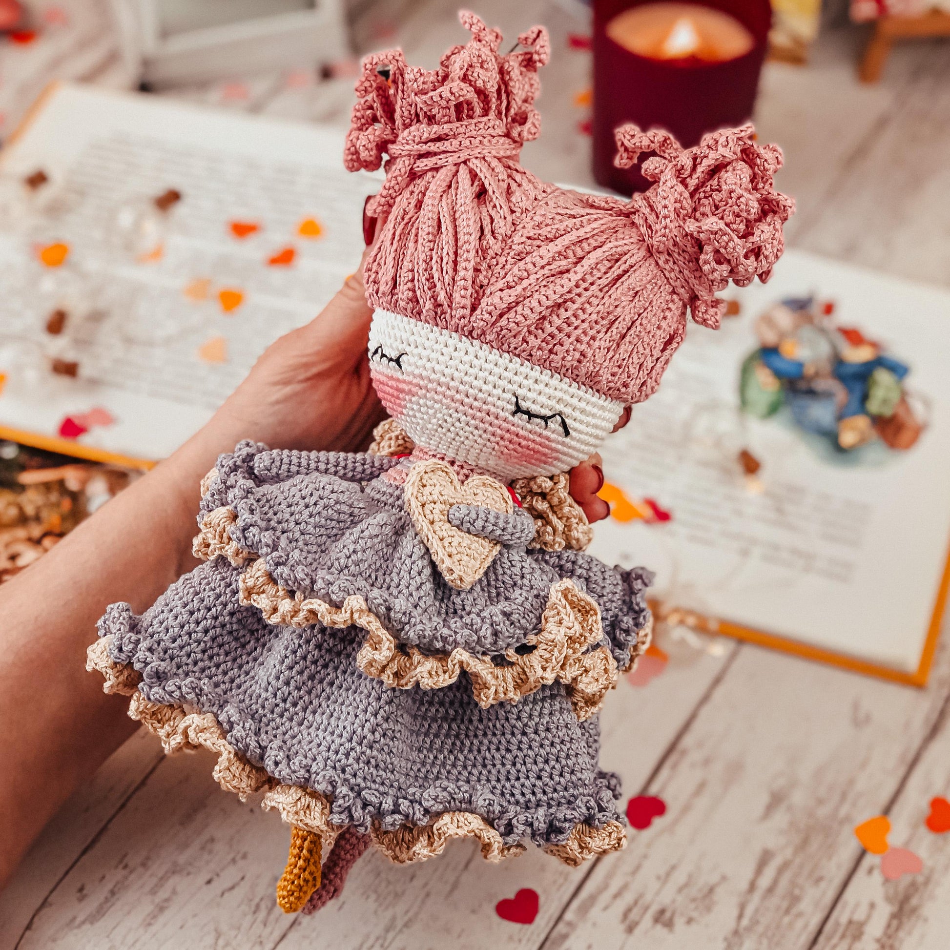 a hand holding a knitted doll in front of a book