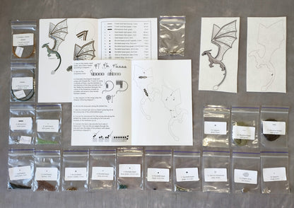 various craft supplies and materials, including bags of beads, a book with instructions, and several printed images of dragon and cat designs.