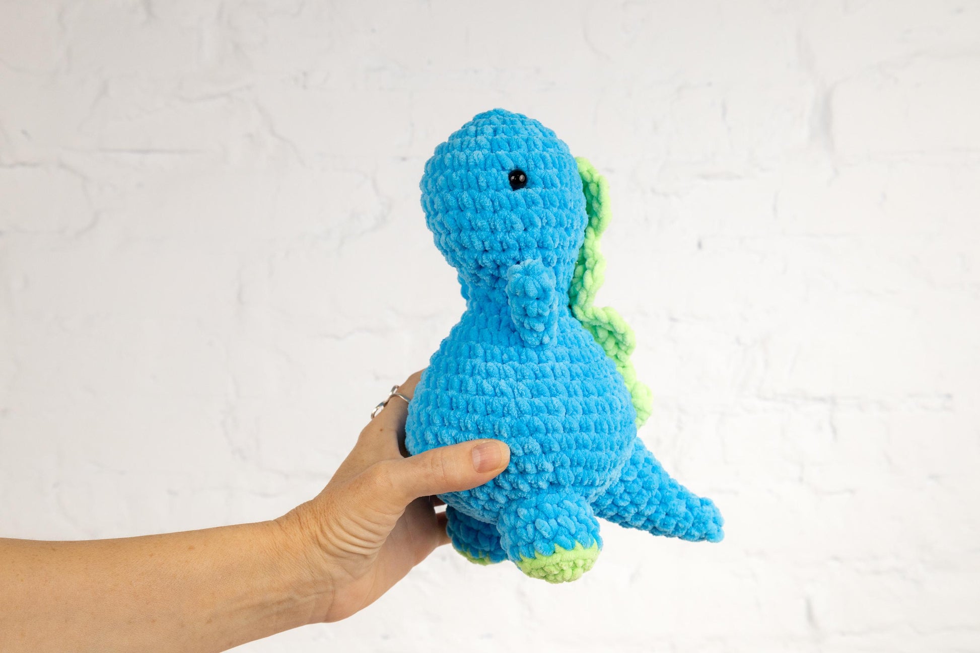a hand holding a crocheted blue and green toy