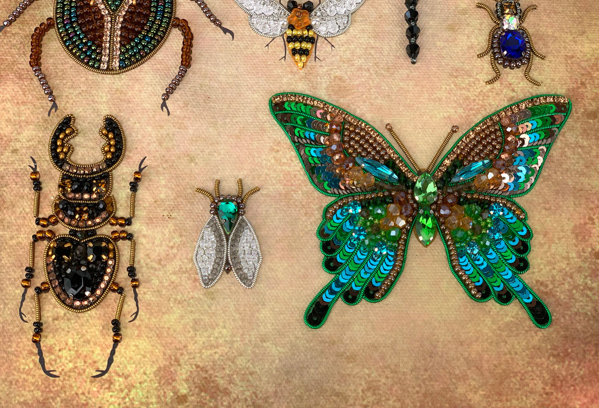 a collection of ornate, intricately designed insect-inspired jewelry, including a butterfly, a beetle, and several other insects, all adorned with colorful gemstones and beads.