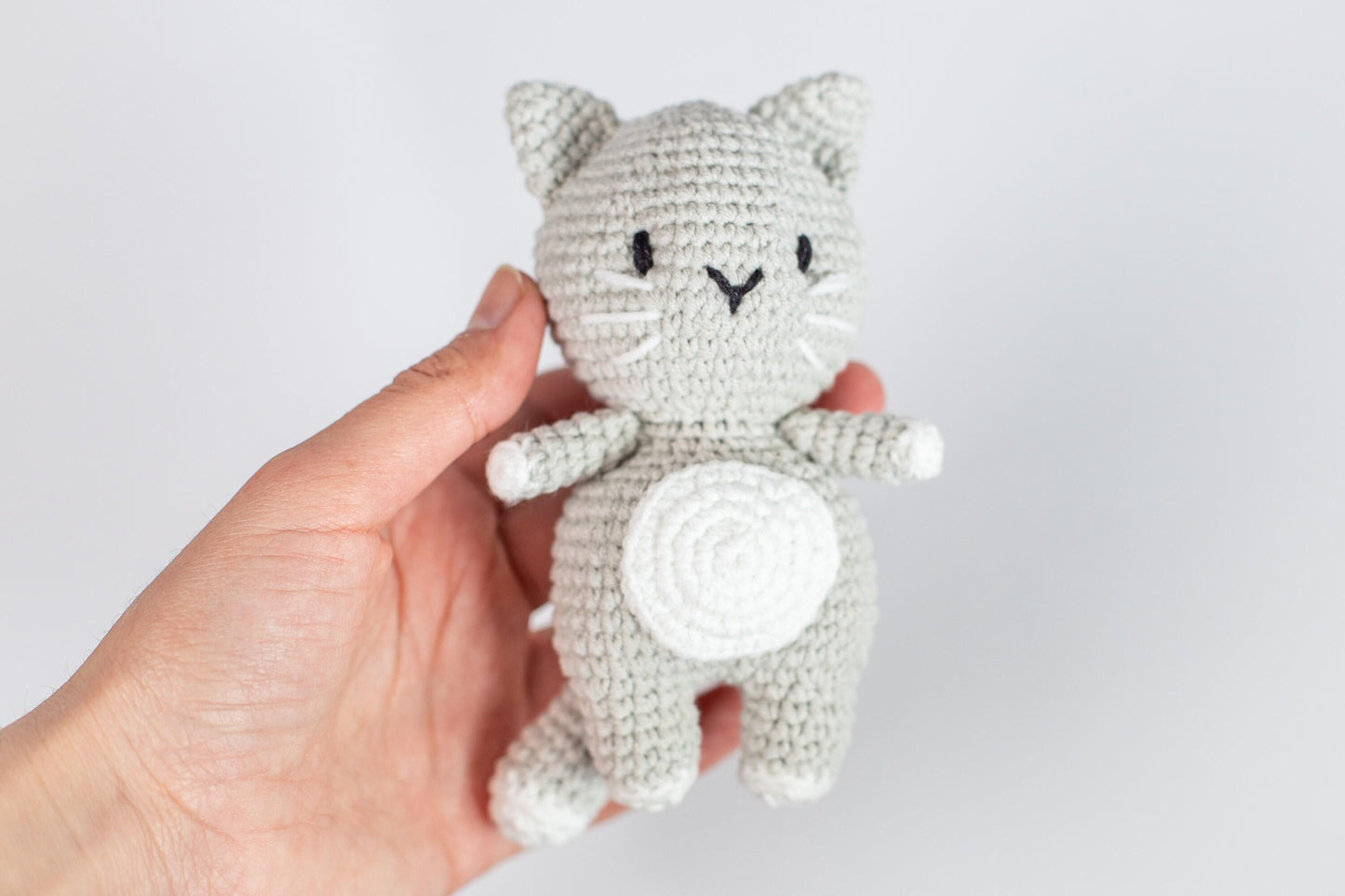 a hand holding a small gray crocheted cat