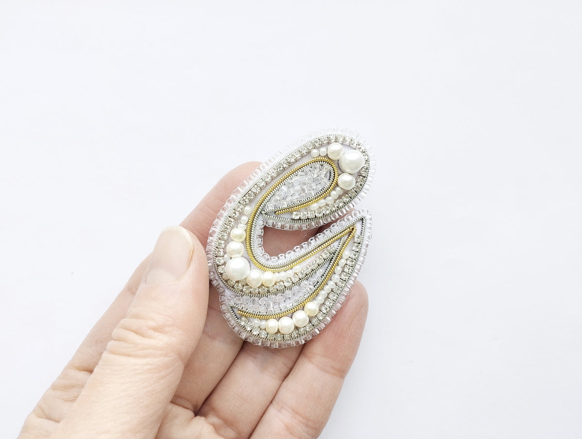 A hand holding a decorative piece of jewelry, which appears to be a brooch or pendant.