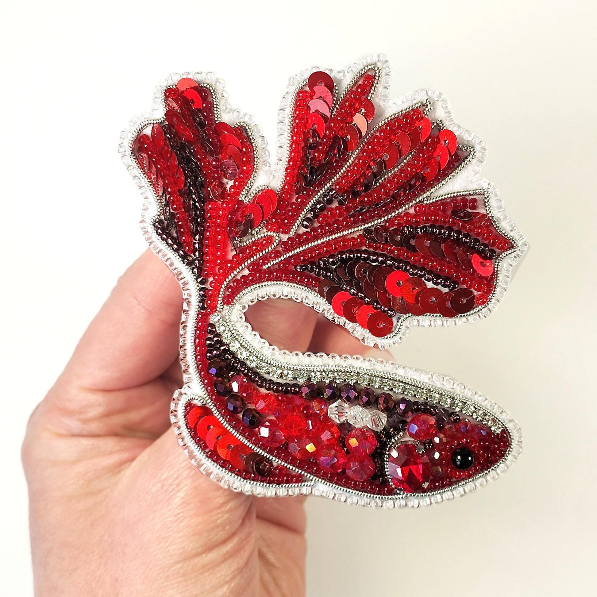 a hand holding a red and white brooch