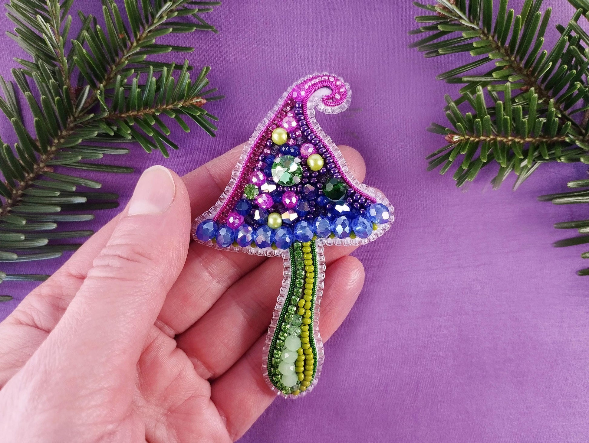 a hand is holding a beaded christmas tree ornament