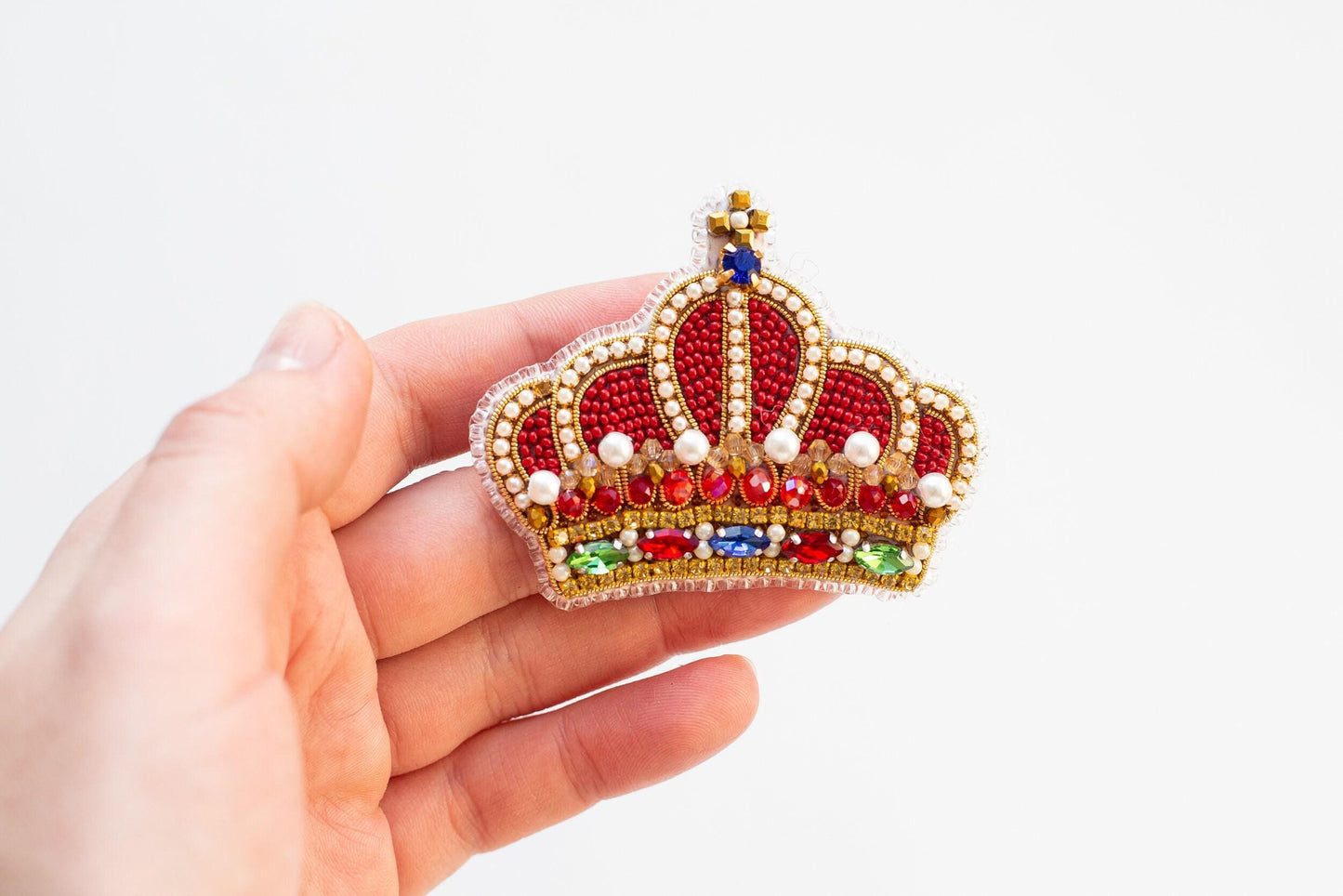 a hand holding a red and gold crown brooch