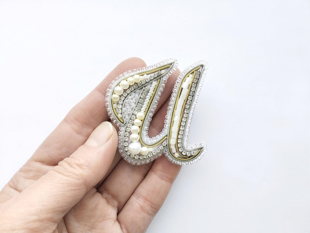 A hand holding a decorative letter 'U' made of beads and pearls.