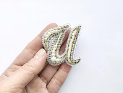 A hand holding a decorative letter 'U' made of beads and pearls.