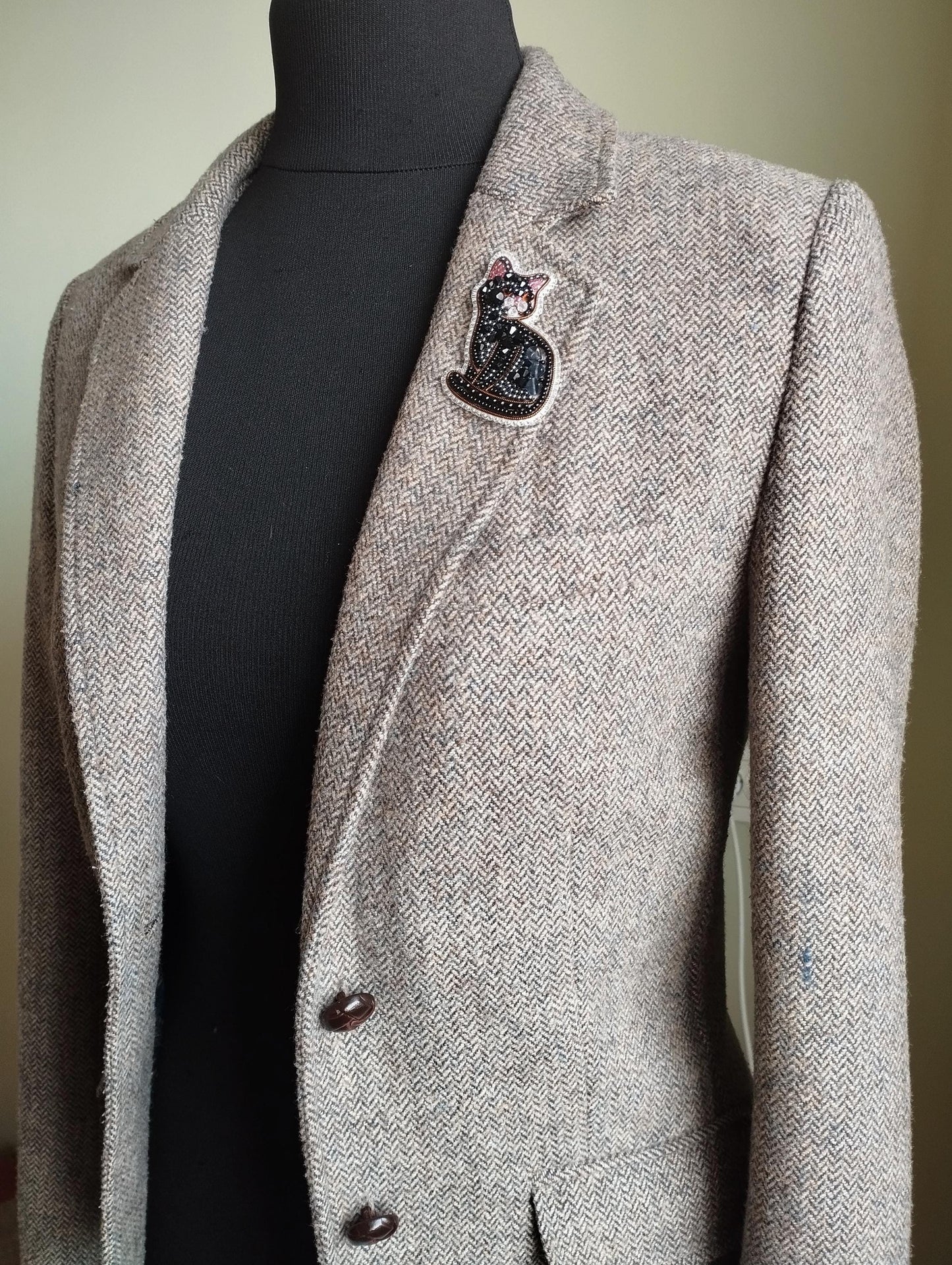 A gray tweed blazer with a black cat pin on the lapel.