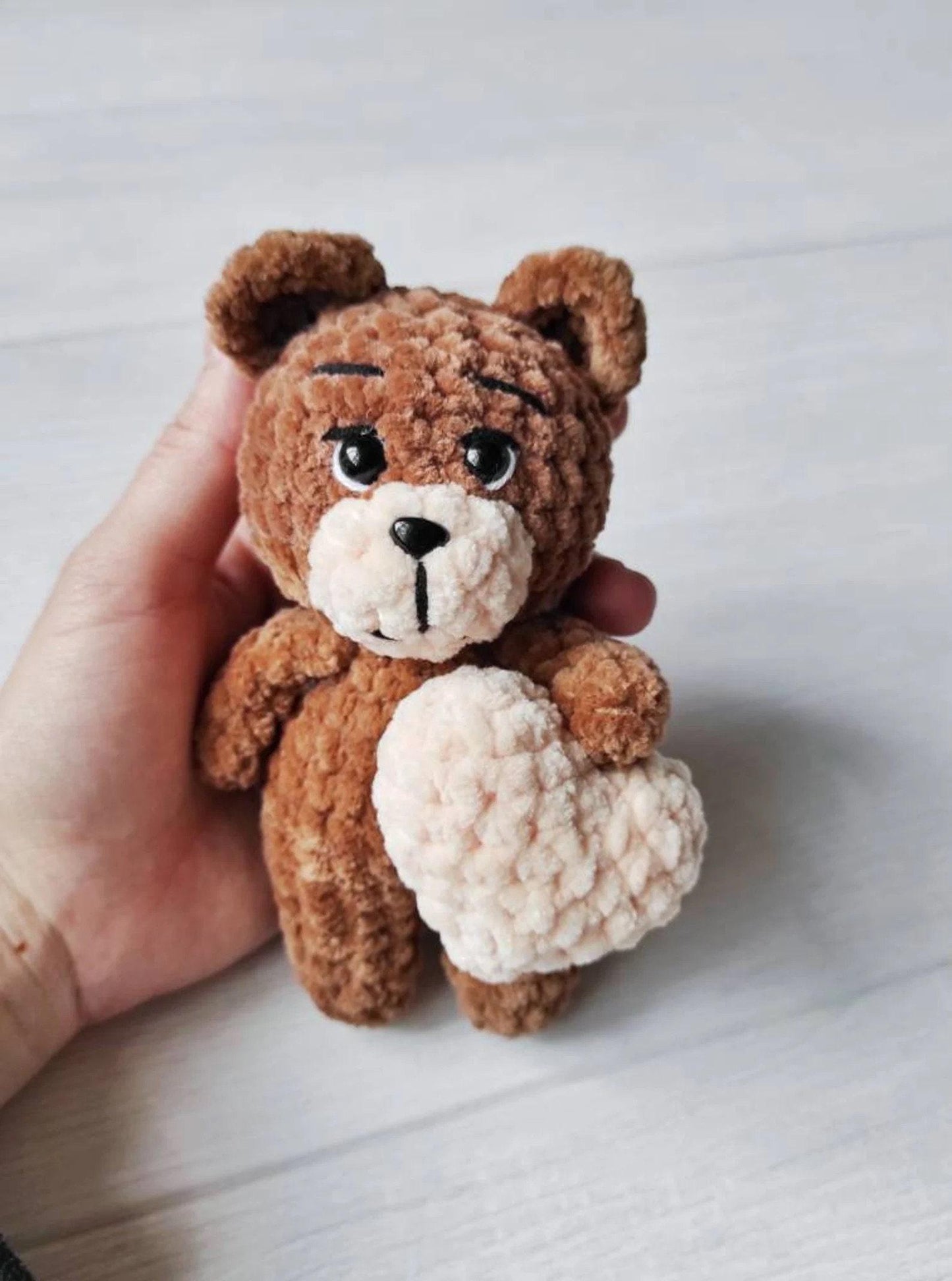 a hand holding a small brown and white teddy bear