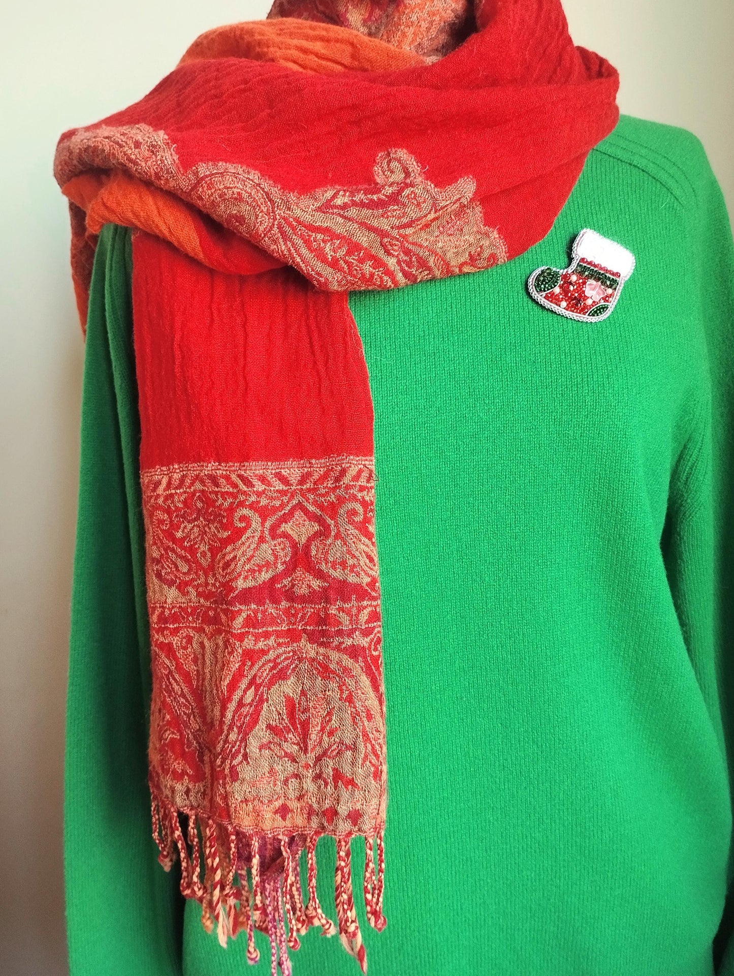 A person wearing a green sweater and a red and gold patterned scarf.
