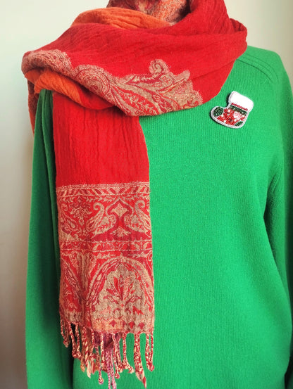 A person wearing a green sweater and a red and gold patterned scarf.