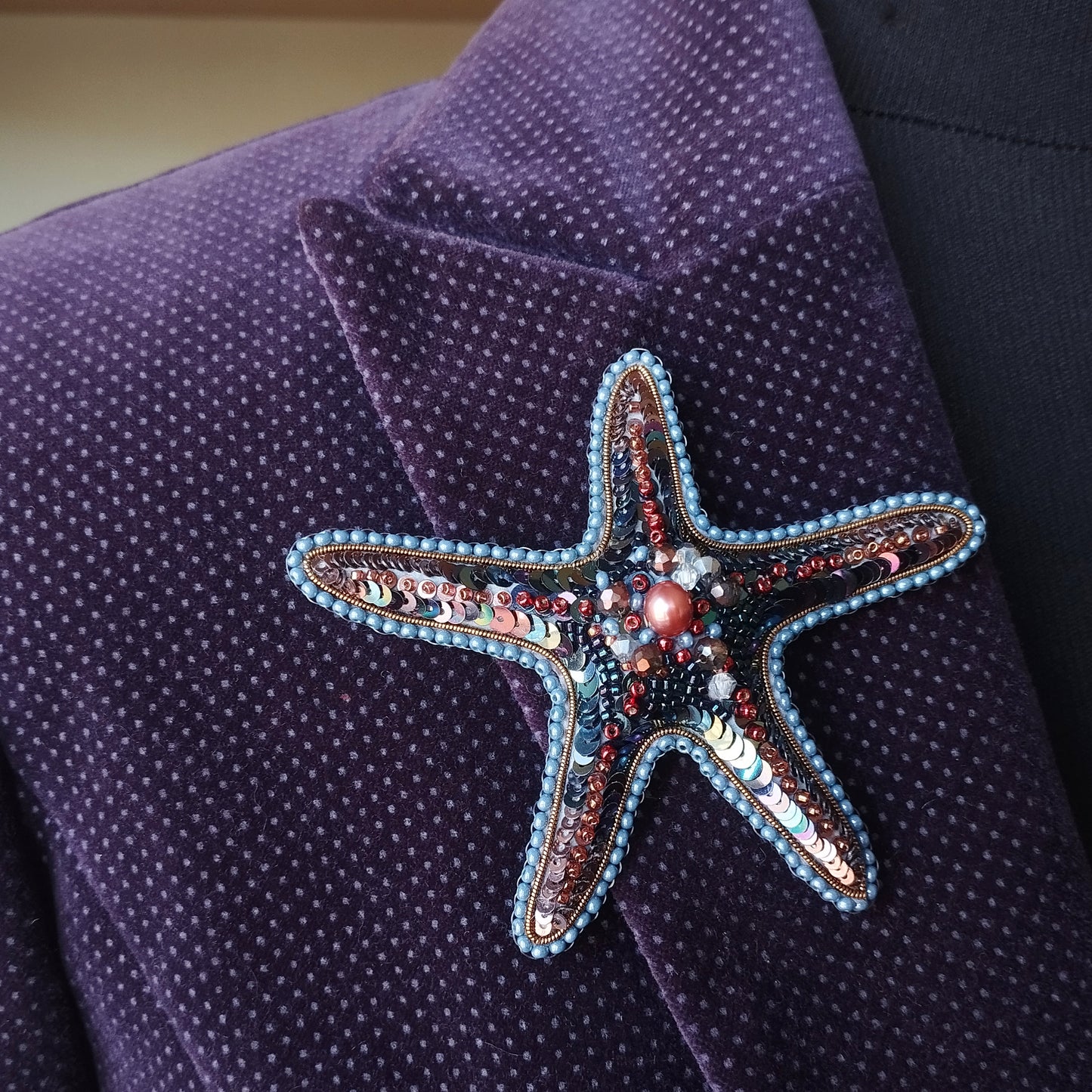 A close-up image of a purple fabric with a starfish-shaped brooch or pin adorned with colorful beads and sequins.