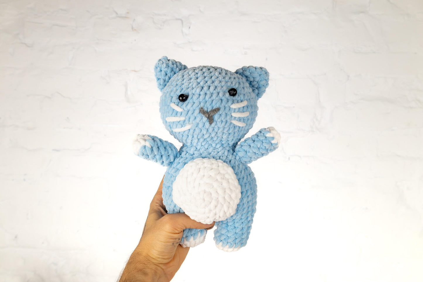 a hand holding a crocheted blue and white cat