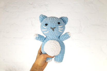 a hand holding a crocheted blue and white cat