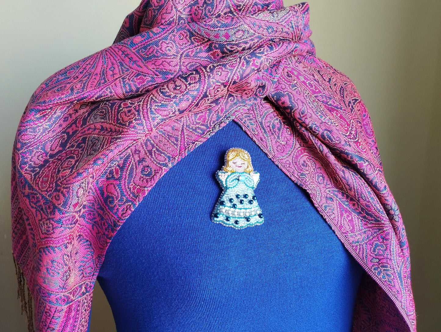 A colorful, patterned scarf is draped over a person's neck, with a small, intricately designed pin or brooch pinned to the chest area.