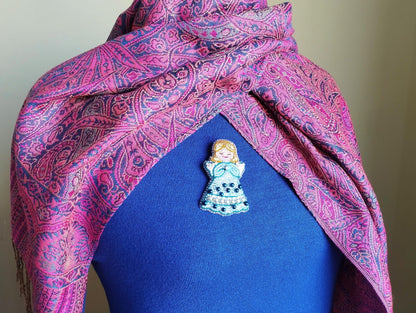 A colorful, patterned scarf is draped over a person's neck, with a small, intricately designed pin or brooch pinned to the chest area.