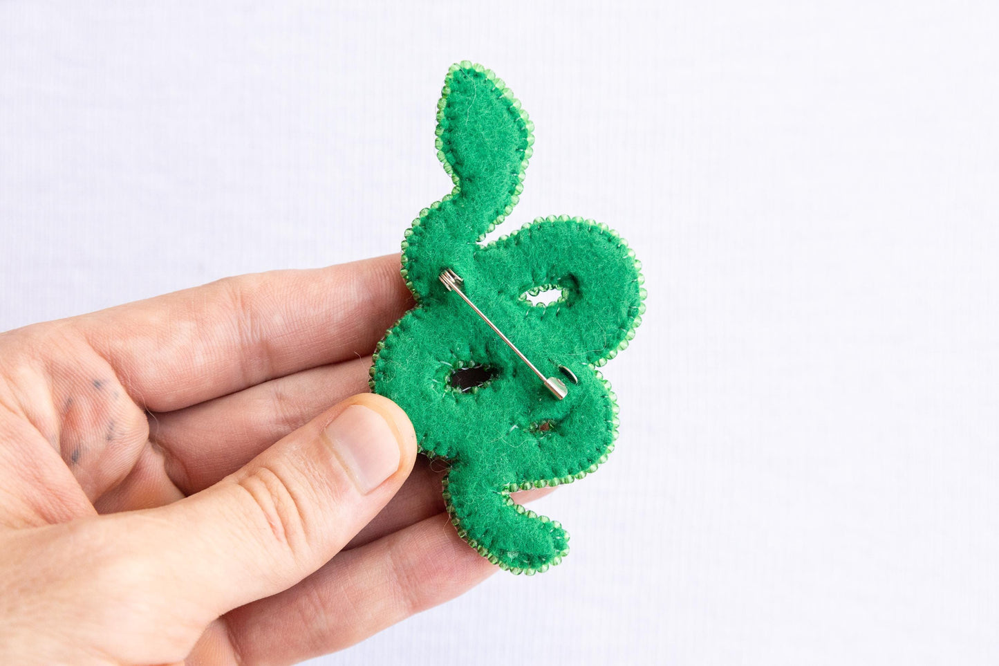 a person is holding a green brooch with a pin in it