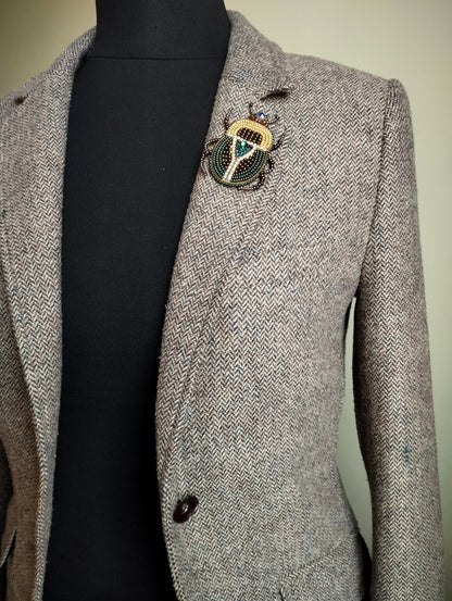 A gray tweed blazer with a decorative brooch on the left breast pocket area.