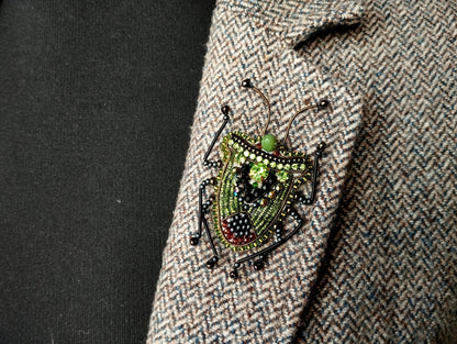 A close-up image of a decorative insect brooch on a tweed jacket lapel.