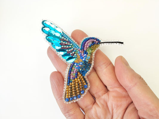 a hand holding a beaded bird ornament