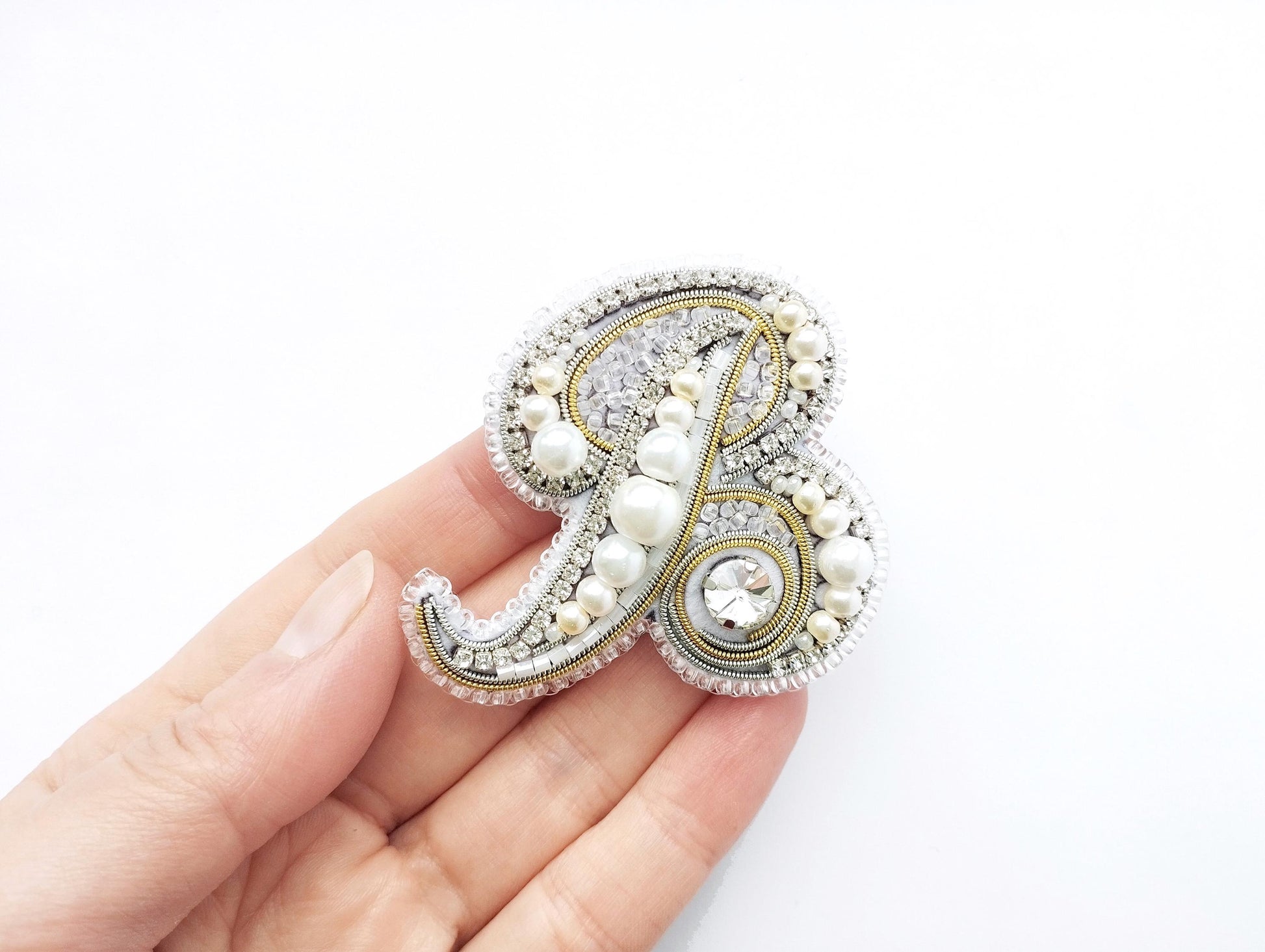 A hand holding a decorative letter p embellished with pearls, diamonds, and rhinestones.