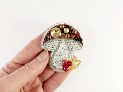 a hand is holding a brooch with beads on it