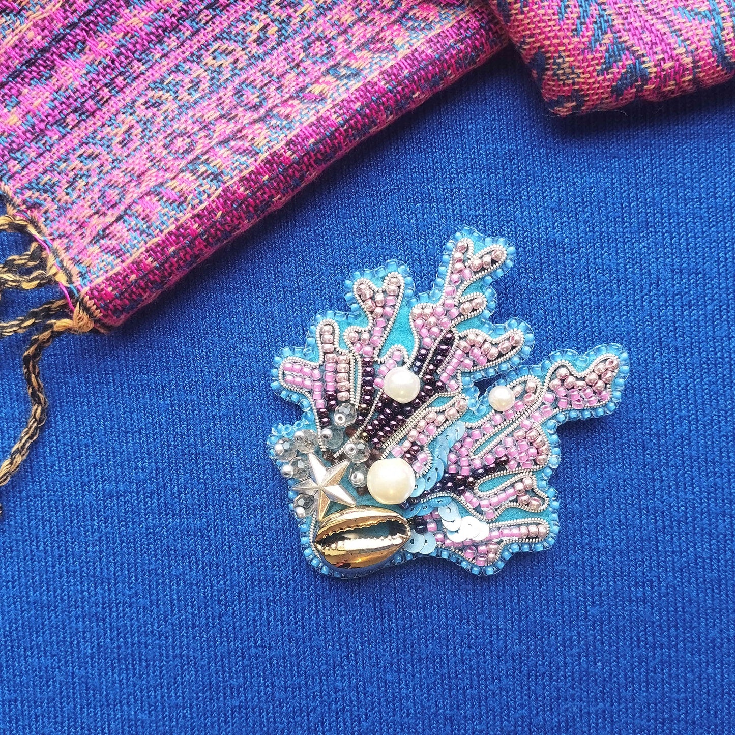 a decorative piece of jewelry, including a beaded coral-shaped brooch, placed on a blue fabric surface.