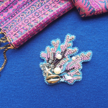 a decorative piece of jewelry, including a beaded coral-shaped brooch, placed on a blue fabric surface.