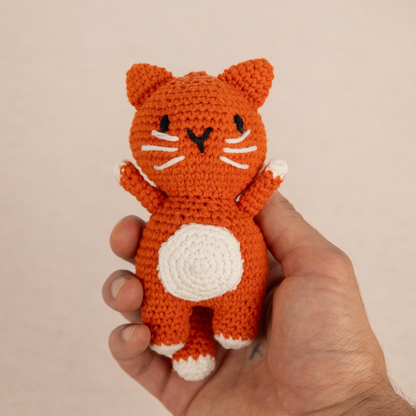 a hand holding a small crocheted orange cat