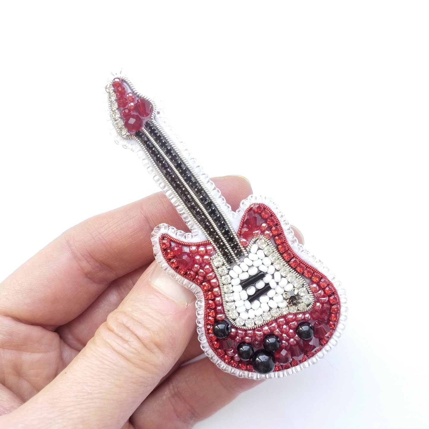 A hand holding a small, intricately designed embroidered guitar brooch.